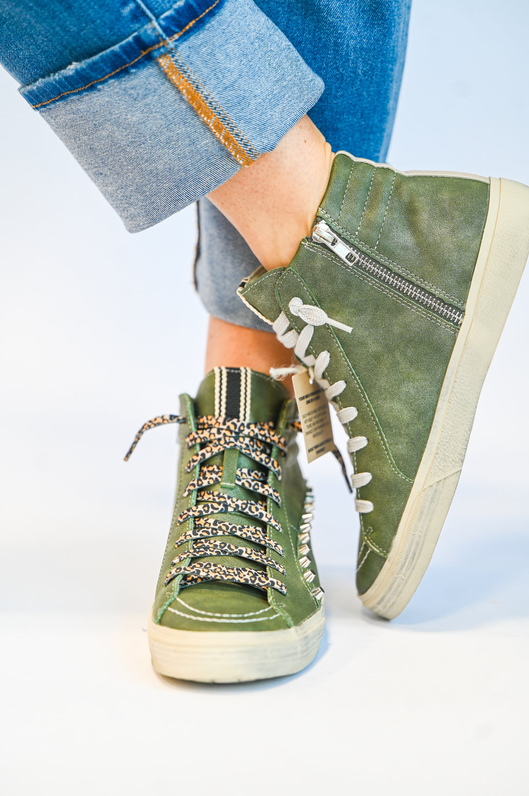 ShuShop olive green high top sneakers with white soles and leopard print laces worn with rolled-up jeans