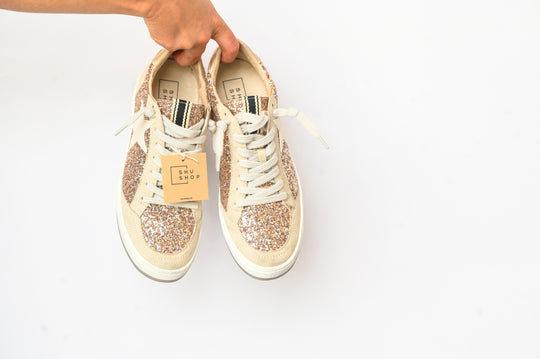Hand holding Paz Champagne Shu Shop Sneakers with glitter and white laces on a white background
