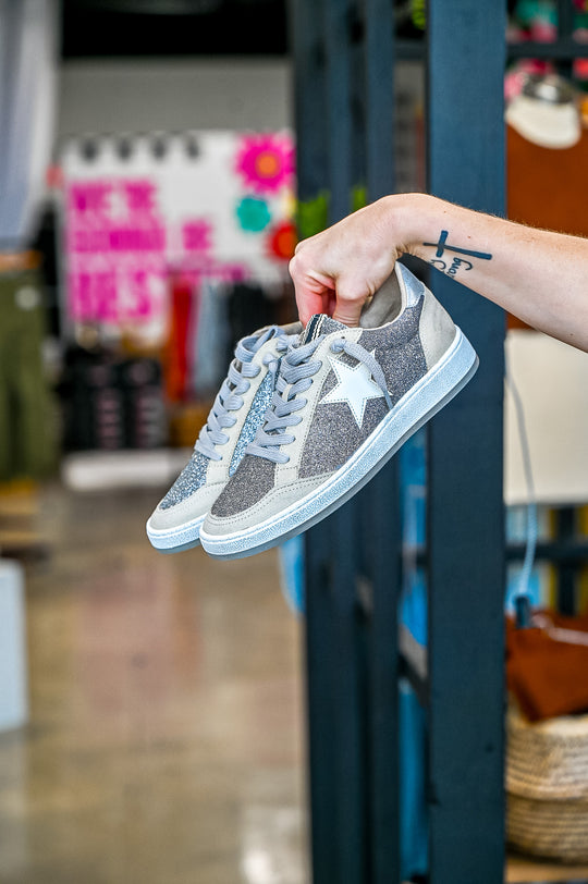 ShuShop Paz Glitter Sneaker in silver glitter with white star and laces held by hand indoors