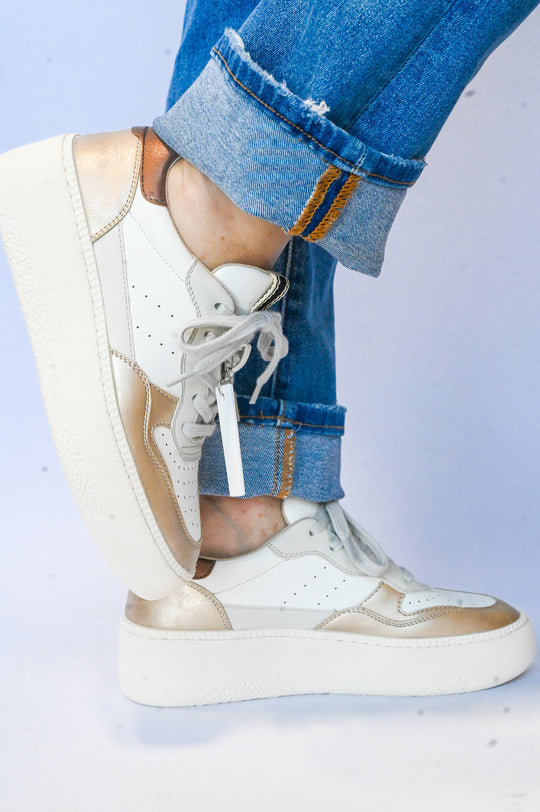 White and gold Sheena Shu Shop sneaker worn with rolled-up blue jeans