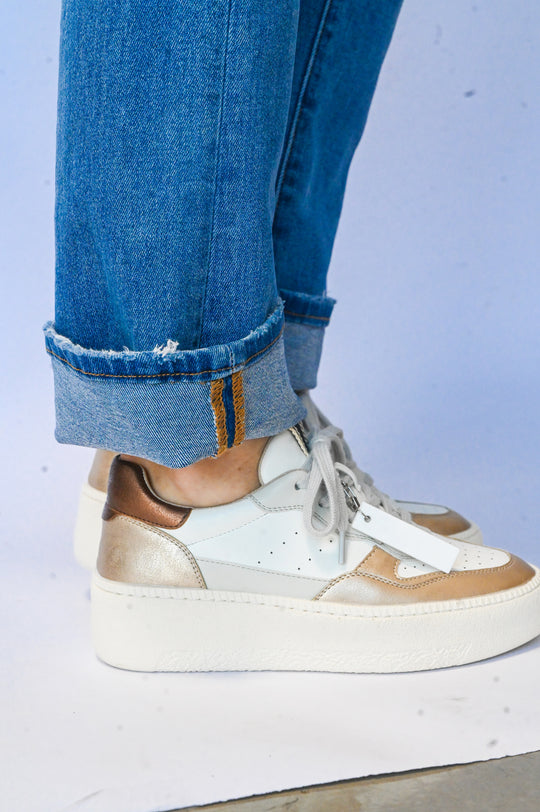 White and gold Sheena Shu Shop sneaker worn with rolled blue jeans featuring a thick white sole