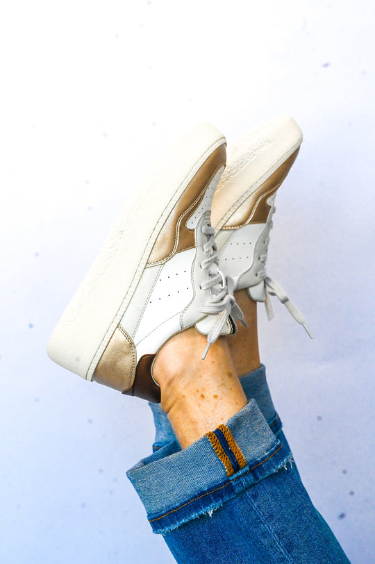 White and gold Sheena Shu Shop sneaker with lace-up design worn with blue rolled jeans