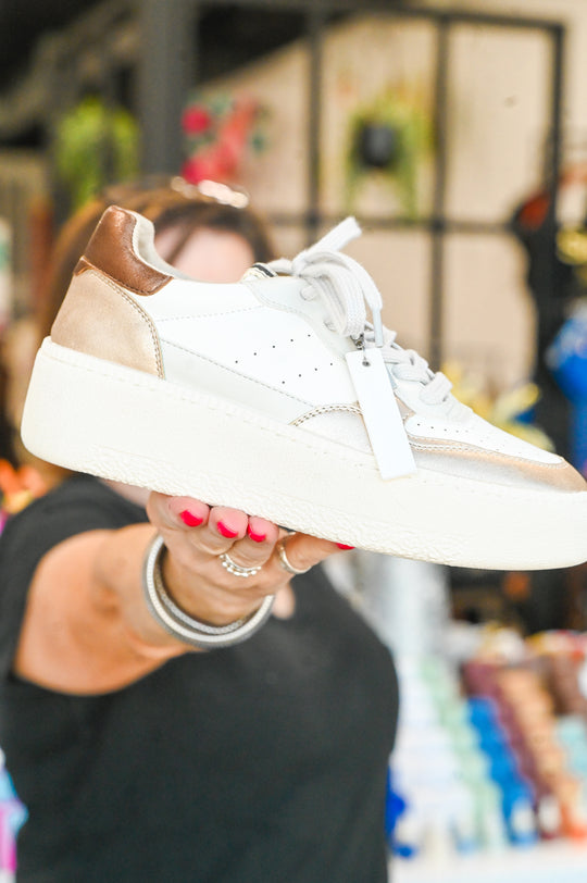 White and beige Sheena Shu Shop sneaker with thick sole and lace-up design held in hand