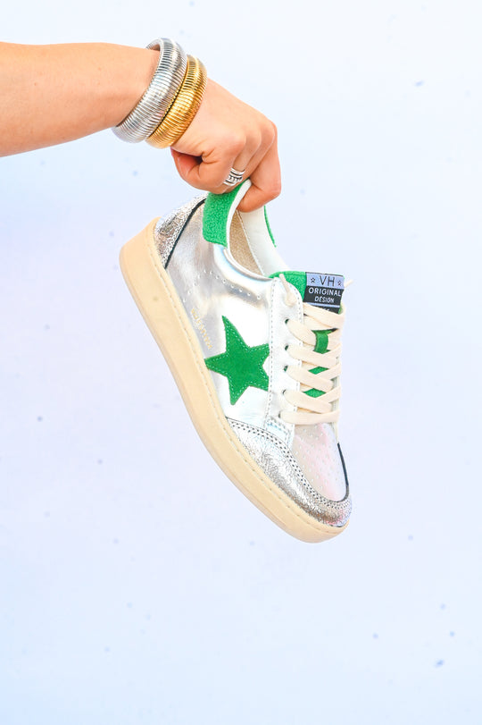 Hand holding metallic silver Vintage Havana sneakers with green star and white laces on white background