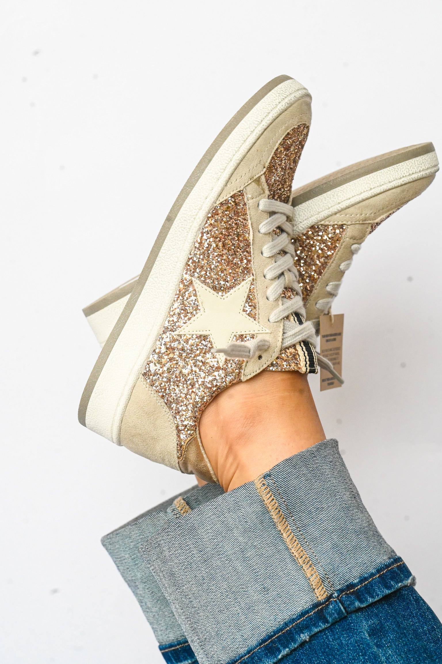 Paz Champagne Shu Shop Sneakers with glitter star design and beige accents worn with rolled denim jeans