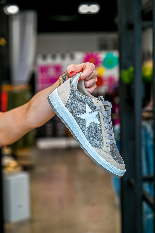 ShuShop Paz Glitter Sneaker in gray with star detail and white sole held by hand