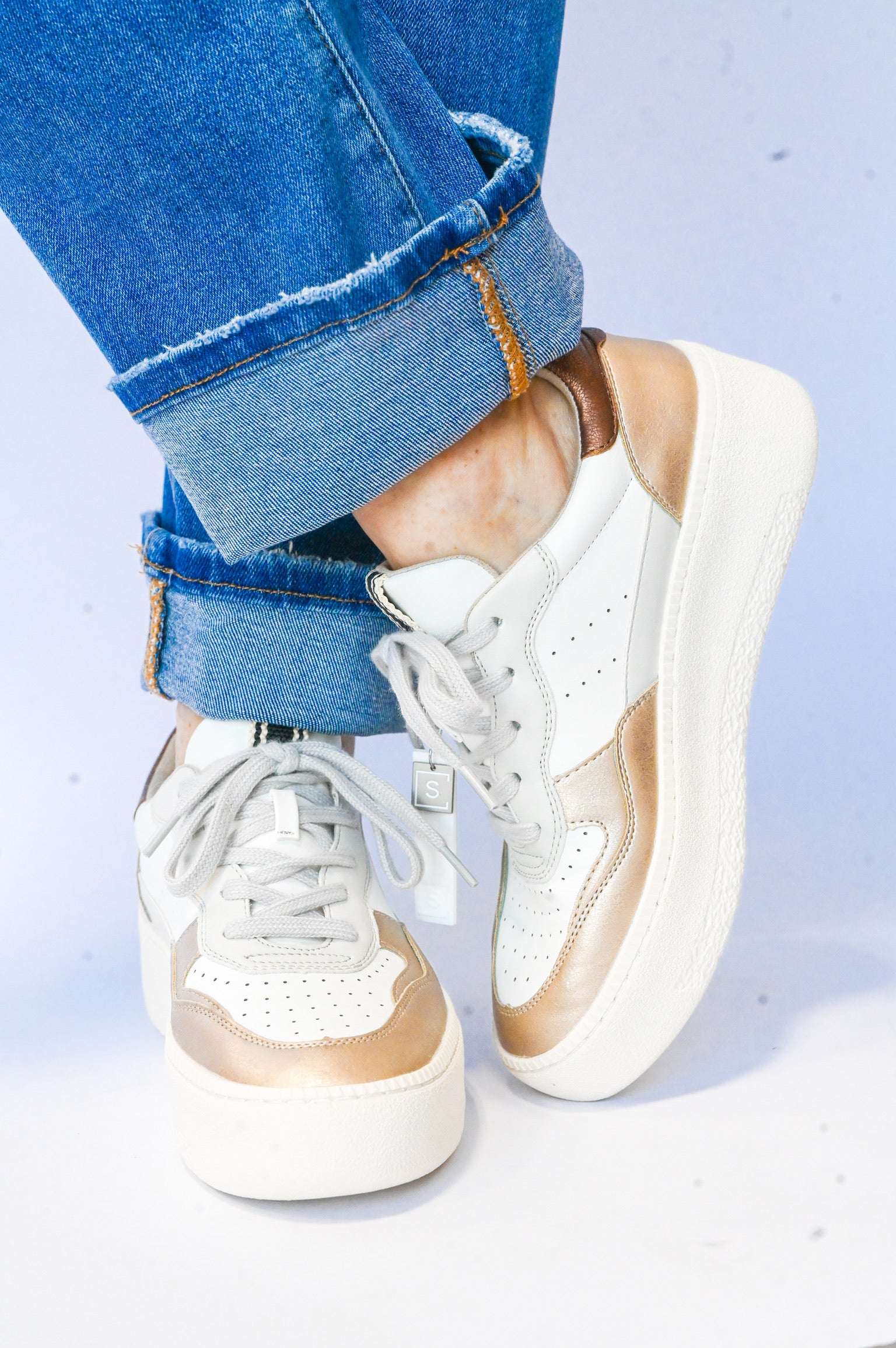 White and gold Sheena Shu Shop sneaker worn with rolled blue jeans casual style